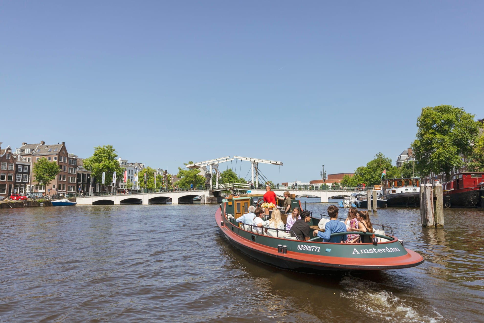 Un bateau de croisière classique plein de passagers navigue sur un canal d'Amsterdam en direction du Magere Brug par une journée ensoleillée.